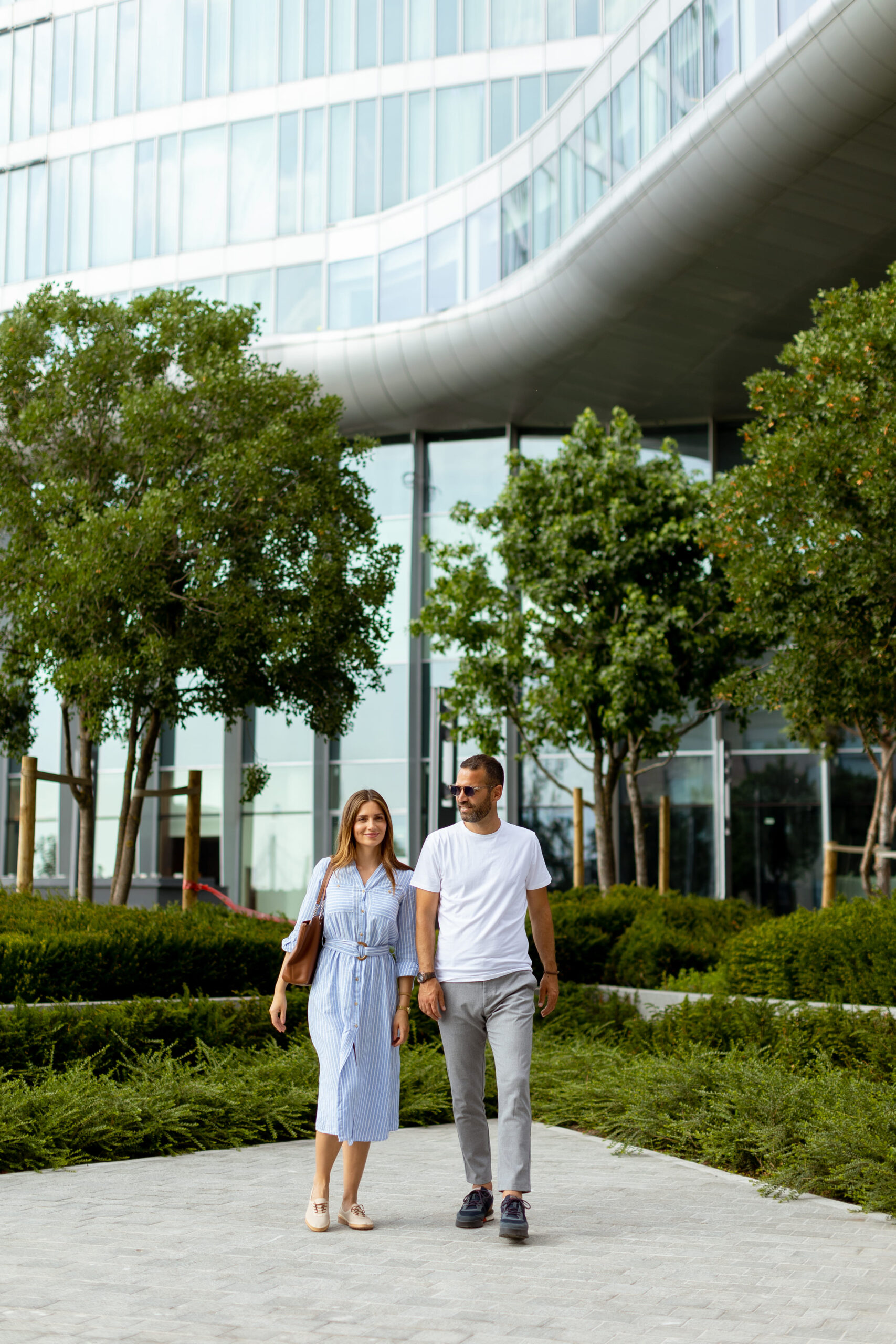 couple-strolls-through-lush-green-landscape-near-modern-architecture-sunny-day (1) (1)